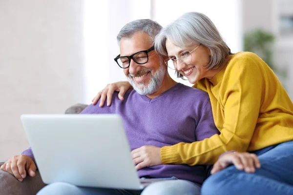 Hermosa pareja de familia madura mirando a la computadora portátil con sonrisa en la cara mientras pasan tiempo juntos — Foto de Stock