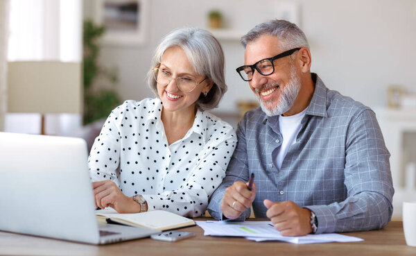 Старшая семья пара учится онлайн вместе дома, глядя на ноутбук, сидя за столом