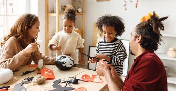 Joven familia afroamericana alegre madre, padre y dos niños preparándose para Halloween en casa —  Fotos de Stock