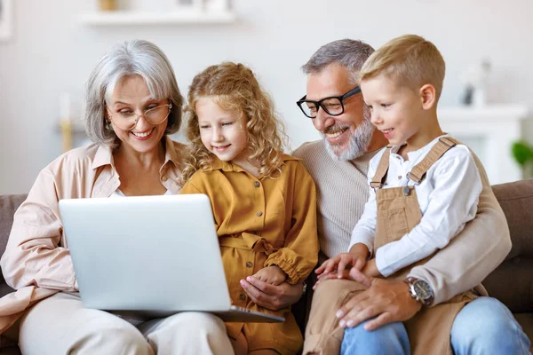 Lachende senior grootouders en schattige kleinkinderen kijken cartoons op laptop — Stockfoto