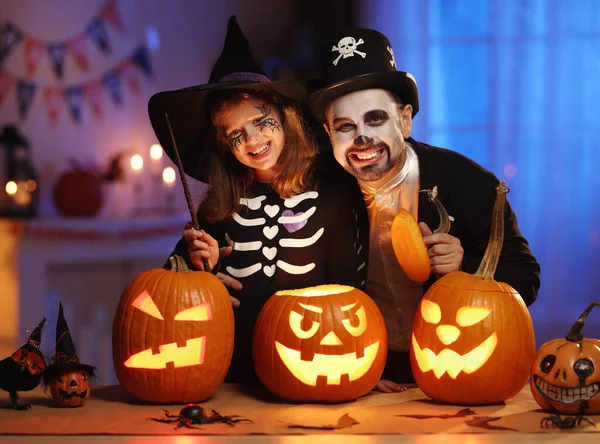 Felice famiglia padre e figlia in costumi di Halloween con jack-o-lanterna incandescente che celebra tutti i santifichi vigilia a casa — Foto Stock