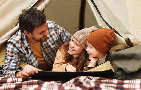 Milující otec a malé děti čtení mapy, zatímco ležel ve stanu v kempu v lese — Stock fotografie
