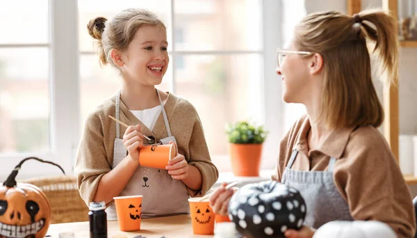 Sonriente madre e hija sentadas en la mesa de madera y haciendo decoración de Halloween juntas en casa — Foto de Stock