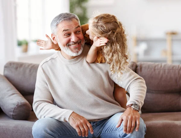 Linda niña cubriendo los ojos con las manos de su abuelo sonriente mientras juegan juntos en casa —  Fotos de Stock