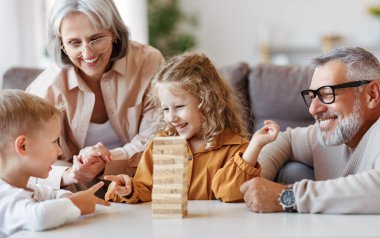 Heyecanlı çocuklar koltukta otururken evde büyük anne ve büyük babalarıyla Jenga oynuyorlar.