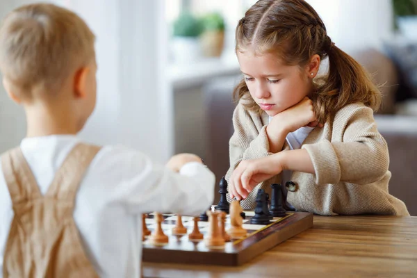 Focused children playing chess game at home while sitting in living room at table with chessboard — Stock Photo, Image