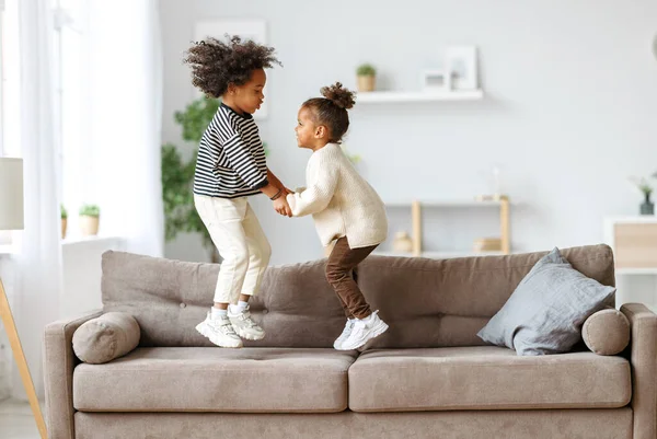 Feliz enérgico crianças afro-americanas saltando no sofá — Fotografia de Stock