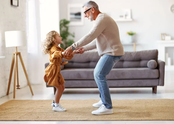 Активный старший дедушка наслаждается танцами с маленькой милой внучкой в гостиной дома — стоковое фото