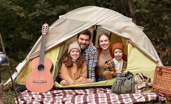 Happy family father, mother and two little children sitting in tent at campsite in forest — Stock Photo, Image