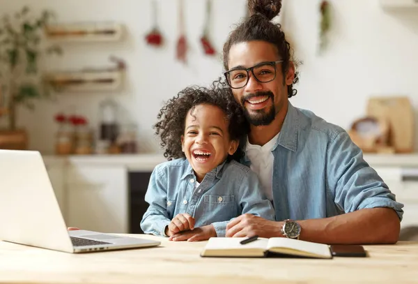 在远程教育期间，快乐的非洲裔美国家庭父亲和儿子与笔记本电脑坐在一起 — 图库照片
