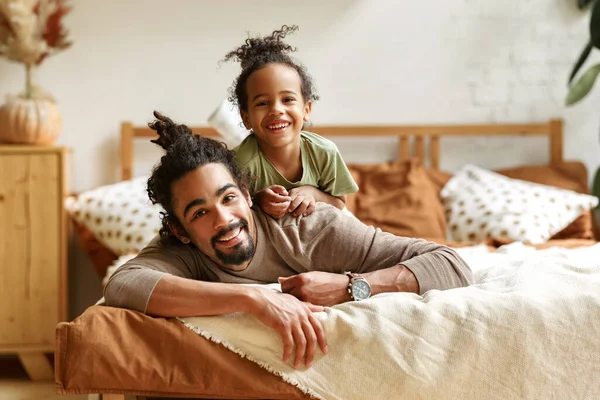 Happy afro american family father and cute little son relaxing at home in bed