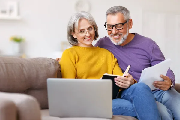 Feliz pareja de ancianos leyendo buenas noticias en la carta, mientras que el pago de facturas en línea en el ordenador portátil — Foto de Stock