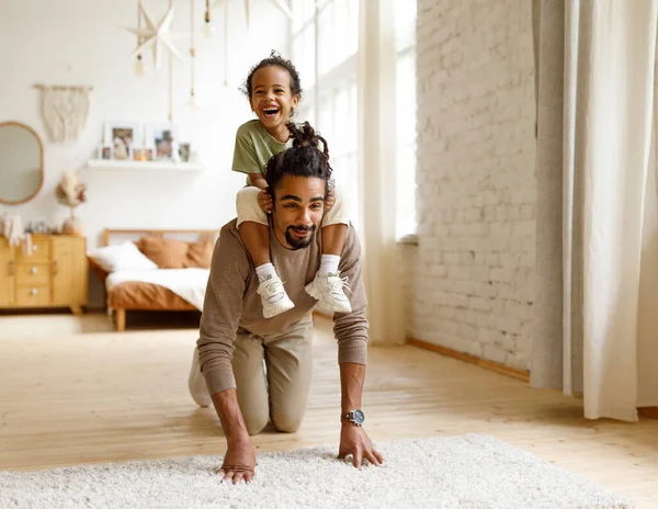 Genç Afro-Amerikan babası, evdeki oyun saatinde küçük oğlunu sırtında taşıyor. — Stok fotoğraf
