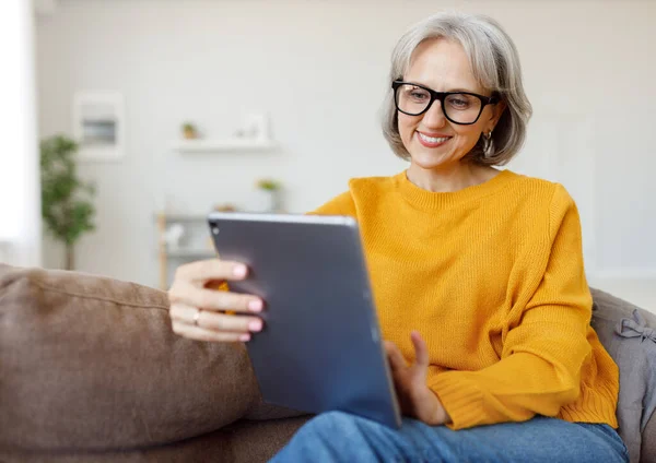 Portrait of happy smiling senior woman resting relaxing on sofa with tablet at home — Stock Photo, Image
