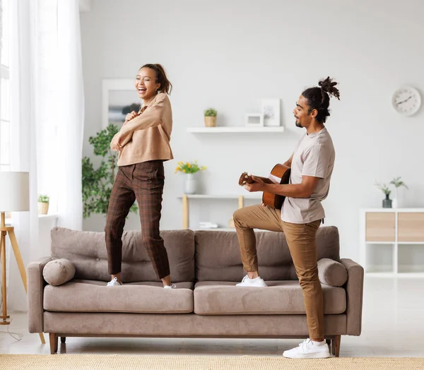 Junges lustiges afrikanisch-amerikanisches Paar spielt am Wochenende zu Hause Gitarre und tanzt — Stockfoto