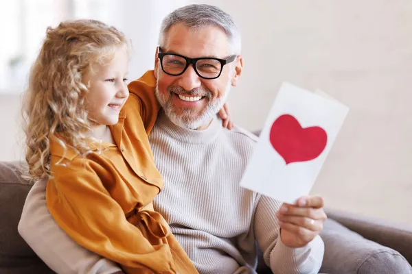 Nettes kleines Mädchen Enkelin gibt handgemachte Grußkarte an lächelnden Großvater zum Geburtstag — Stockfoto
