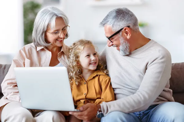 Mosolygó idősebb nagyszülők és aranyos kislány unoka néz rajzfilmeket laptopon — Stock Fotó
