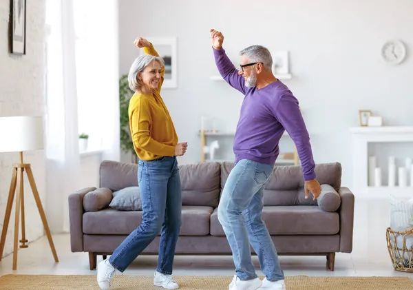 Energisk senior familj par dansar tillsammans i vardagsrummet hemma, flytta till musik Stockbild