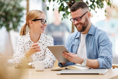 Kahve molası sırasında sohbet eden iki pozitif iş arkadaşı dijital tablete bakıyor.