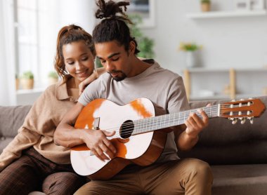 Genç, gülümseyen Afrikalı Amerikalı müzisyen mutlu kız arkadaş için gitarda enstrümantal müzik çalıyor.