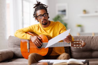 Kağıt üzerinde klasik akustik gitar okuma notalarıyla odaklanmış Afro-Amerikan erkek müzisyen.
