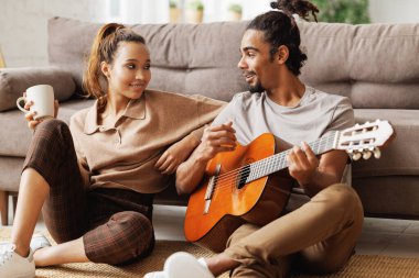 Genç, gülümseyen Afrikalı Amerikalı müzisyen mutlu kız arkadaş için gitarda enstrümantal müzik çalıyor.