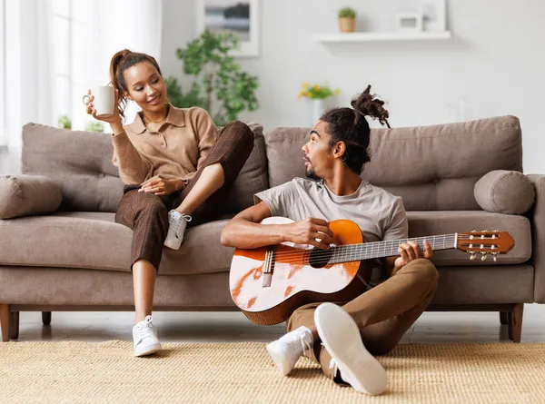 Jovem bela família afro-americana casal tocando guitarra acústica em casa — Fotografia de Stock