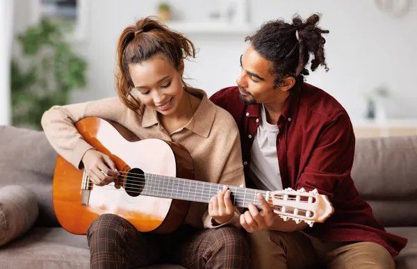 Hafta sonları evde dinlenirken kanepede oturup erkek arkadaşına gitar çalan melez bir kadın.