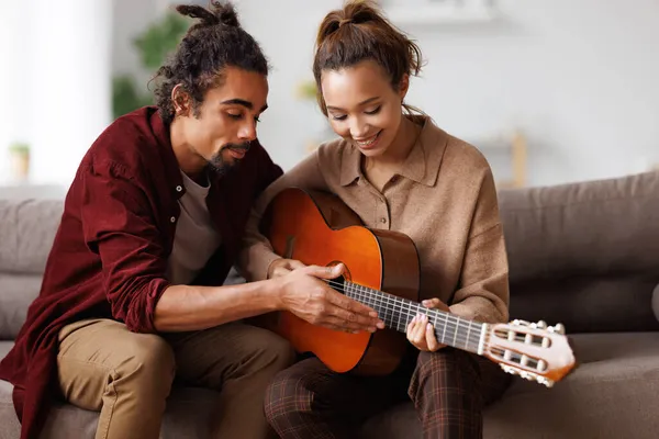 Genç Afrikalı Amerikalı erkek kız arkadaşına evde akustik gitar çalmasını öğretiyor.