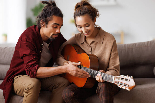 Young african american man teaching girlfriend to play acoustic guitar at home
