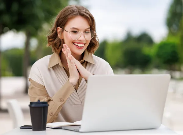 Glückliche junge Lehrerin in formalem Outfit und Brille gibt Unterricht online sitzend mit Laptop draußen — Stockfoto