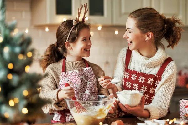 Linda niña ayudando a la madre a hacer masa para galletas de Navidad en la acogedora cocina en casa —  Fotos de Stock