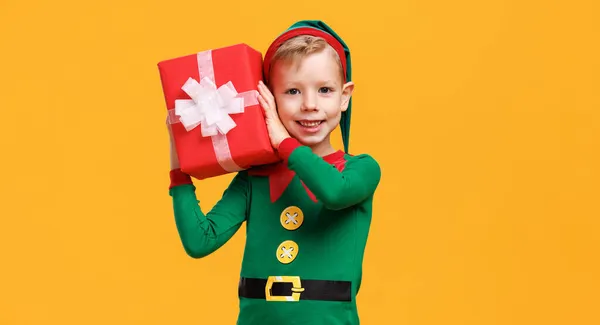 Exultante menino caucasiano pré-escolar vestindo traje de duende de Natal segurando presente de Natal — Fotografia de Stock