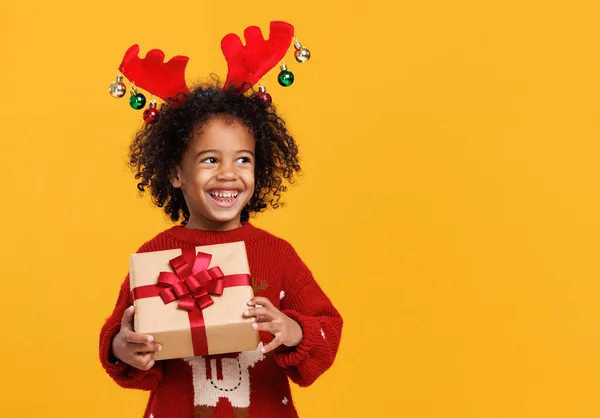 Vacanze di Natale. Felice piccolo ragazzo africano americano che indossa corna di cervo rosso con scatola regalo di Natale — Foto Stock