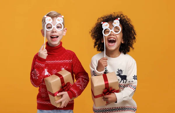 Glada flerrasiga barn i varma stickade tröjor som håller julfest glasögon och presentaskar — Stockfoto