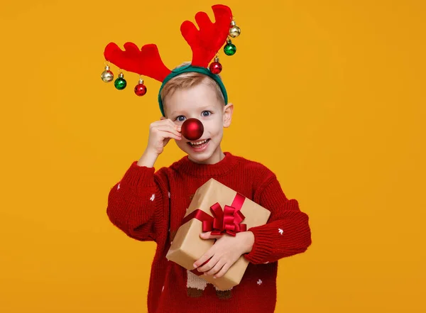 Menino alegre com presente de Natal embrulhado segurando bola de árvore de Natal vermelho na frente de seu nariz — Fotografia de Stock