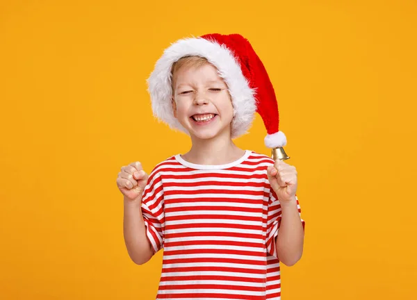 Glad liten pojke står i Santa hatt med slutna ögon, knyta knytnävar samtidigt som julen önskar — Stockfoto