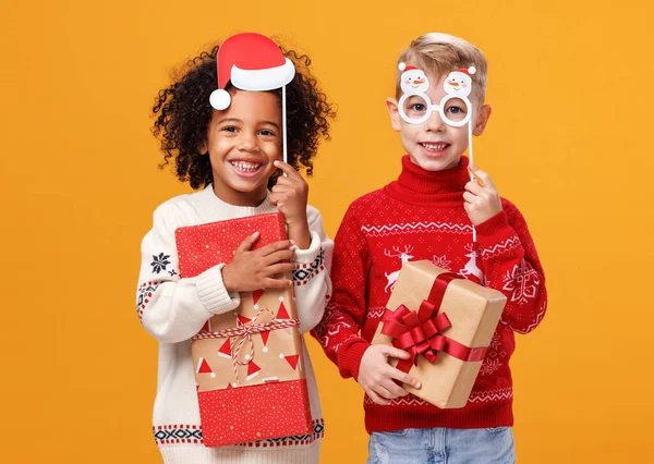 Felici bambini multirazziali in maglioni a maglia caldi che tengono bicchieri da festa di Natale e scatole regalo — Foto Stock