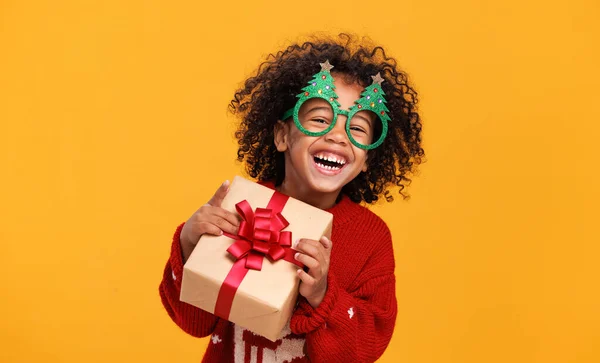 Happy little african american boy wearing funny glasses in form of Christmas trees with xmas gift — Stock Photo, Image