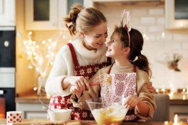Sevimli küçük kız, annesinin evde rahat bir mutfakta Noel kurabiyesi yapmasına yardım ediyor.