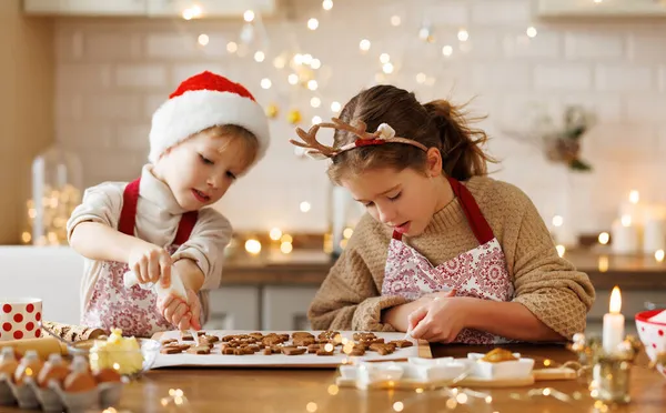 Šťastné děti chlapec a dívka s úsměvem při zdobení vánoční perníčky v kuchyni — Stock fotografie