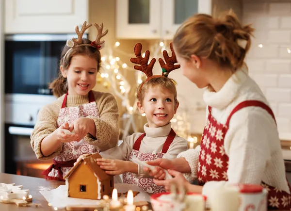 Feliz familia madre y dos niños en delantales de Navidad decorando la casa de jengibre miel de Navidad — Foto de Stock