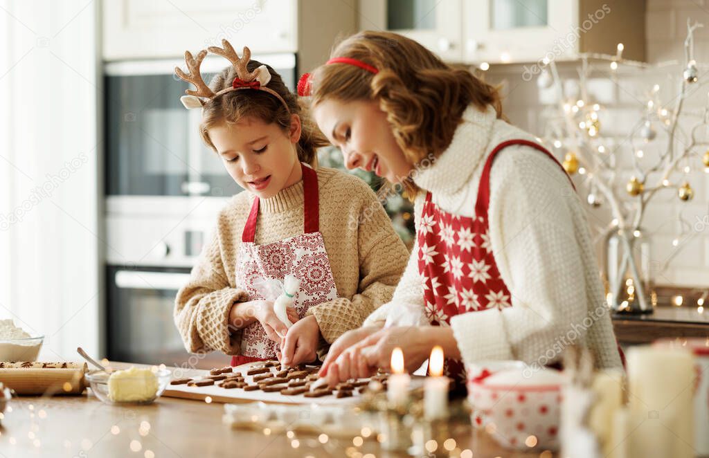 Happy family mother and girl daughter decorating Christmas gingerbread cookies after baking