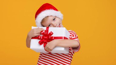 Kırmızı Noel Baba şapkalı sevimli çocuk elinde uzun zamandır beklenen Noel hediyesini tutuyor.