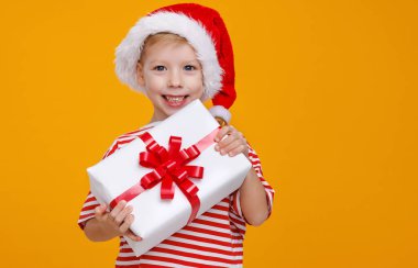 Kırmızı Noel Baba şapkalı sevimli çocuk elinde uzun zamandır beklenen Noel hediyesini tutuyor.