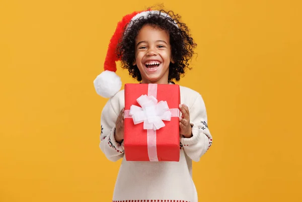 Feliz menino afro-americano encaracolado em chapéu de santa e camisola de malha abraçando grande caixa de presente de Natal firmemente — Fotografia de Stock