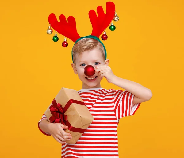 Alegre niño pequeño con regalo de Navidad envuelto sosteniendo bola de árbol de Navidad rojo en frente de su nariz — Foto de Stock