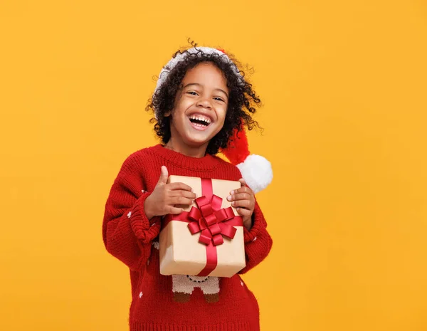 Szczęśliwy mały afro amerykański kręcone chłopiec w Santa kapelusz i dzianiny sweter przytulanie duży świąteczny prezent pudełko szczelnie — Zdjęcie stockowe