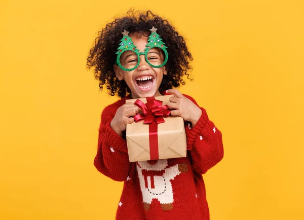 Happy little african american boy wearing funny glasses in form of Christmas trees with xmas gift — Stock Photo, Image