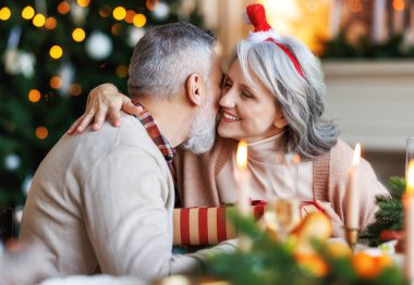 Mutlu son sınıf aile çifti evde şenlikli bir akşam yemeği sırasında birbirlerine sarılıp Noel hediyelerini veriyorlar.